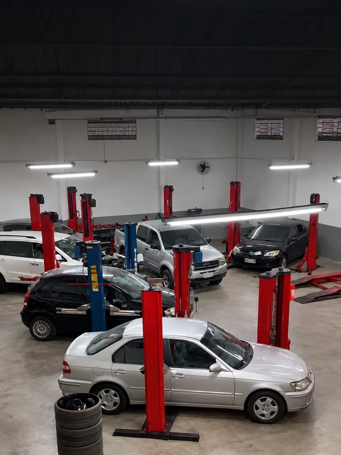 Interior da oficina Fazam Car, com veículos e elevadores; imagem editada para remover textos promocionais
